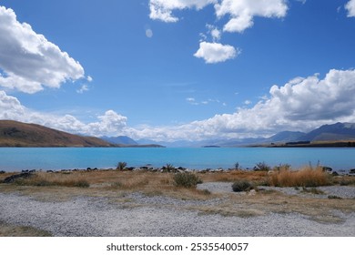 Scenic View of Lake Tekapo with Vibrant Blue Water on a Sunny Summer Day, Surrounded by Rocky Shoreline and Golden Grass under Clear Blue Sky – South Island, New Zealand - Powered by Shutterstock