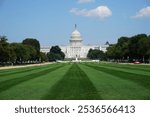 Scenic view of the landmark United States Capitol building in Washington DC from a green meadow on the National Mall on a sunny day under a blue sky; tourism and sightseeing in the American capital.