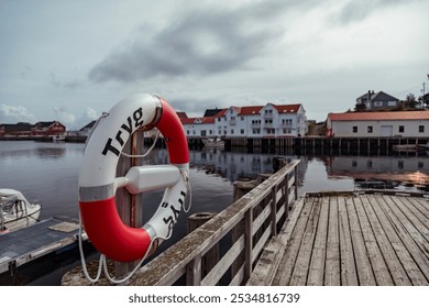 Scenic View of a Lifebuoy on the Dock in Henningsvær, Lofoten Islands, Norway, Surrounded by Boats and Vibrant Buildings Under a Cloudy Sky - Powered by Shutterstock