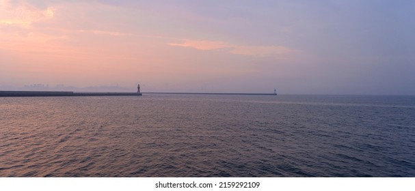 A scenic view of a lighthouse in the port of Dalian on a sunset sky background