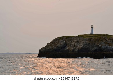 Scenic view of a lighthouse standing atop a rocky coastline with calm ocean waves reflecting the soft sunset glow, creating a tranquil maritime scene. - Powered by Shutterstock