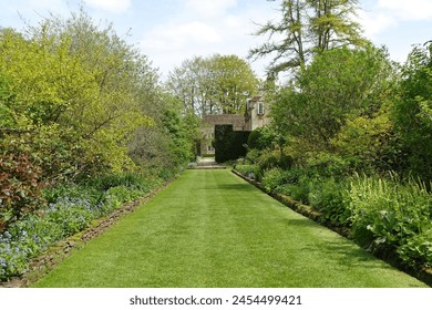 Scenic view of a lush green grass lawn path through an attractive English style landscape garden with leafy plants and colourful flowers - Powered by Shutterstock