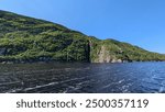 A scenic view of a lush, green hillside that slopes down to meet the dark, rippling waters of  Saguenay River.The water in the foreground is slightly disturbed,indicating movement from a passing boat.