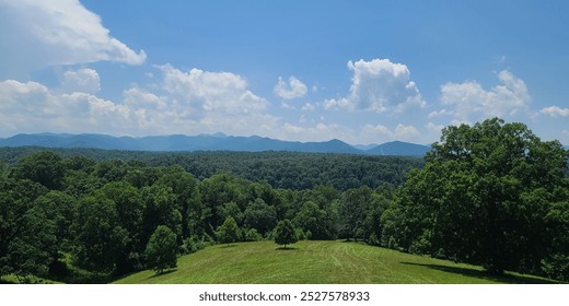 A scenic view of a lush green landscape with rolling hills and distant mountains under a clear blue sky with scattered clouds. - Powered by Shutterstock