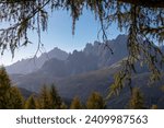 Scenic view of majestic mountain peaks Cima Bagni and Hochbrunnerschneid, Sexten Dolomites, South Tyrol, Italy, Europe. Hiking concept Italian Alps. Blue sky. Vista through golden autumn tree branches