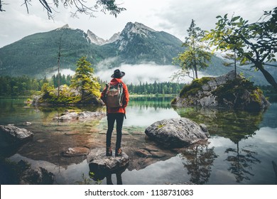 Scenic view of a man wearing a red jacket, a hat and a backpack looking at mountains, Lake Hintersee, Berchtesgaden, Germany  - Powered by Shutterstock