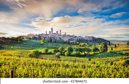 Scenic view of the medieval town of San Gimignano in beautiful scenery with vineyards in beautiful golden evening light with blue sky and clouds at sunset in summer, Tuscany, province of Siena, Italy