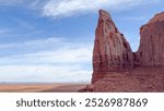 Scenic view in Monument Valley, Arizona. A slender spire of red rock known as Spearhead Mesa stands out against a blue sky. The vast desert landscape stretches out in the background - USA