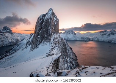 Scenic View from Mount Hesten on Iconic Mountain Segla at dawn in winter with snow in front of colorful sky and mountain range in background, Fjordgard, Senja, Norway
