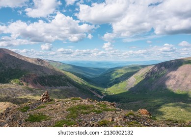 Scenic view from mountain pass to green forest valley among mountain ranges and hills on horizon at changeable weather. Green landscape with sunlit mountain vastness under cumulus clouds in blue sky.