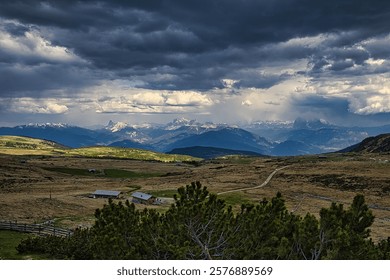 Scenic view of mountains under dramatic cloudy sky with lush green fields, showcasing nature's beauty and contrast.