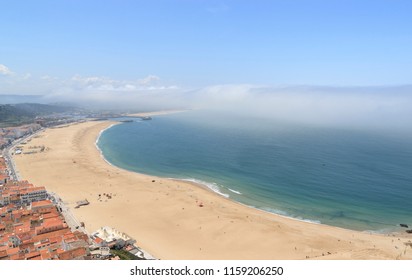 Scenic View Of Nazare Beach. Coastline Of Atlantic Ocean. Portuguese Seaside Town On Silver Coast. The Clouds Above The Water Are Like Tsunami Waves. Nazare, Portugal. Summer Sunny Day. 