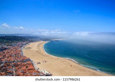 Scenic View Of Nazare Beach, Portugal. Coastline Of Atlantic Ocean. Portuguese Seaside Town On Silver Coast. White Houses With Red Roofs Cityscape. The Clouds Above The Water Like Tsunami Waves. 