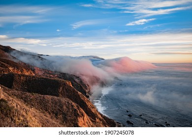 Scenic View Of Ocean Shore Near Big Sur, California, USA. Cloud Covered Coast, Sea And Cliff Hills. Foggy Pink Sunset Landscape.