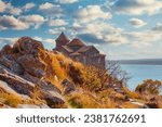 Scenic view of the old Hayravank Monastery on the shores of Armenian Lake Sevan on a sunny autumn day, blue sky and fluffy clouds.