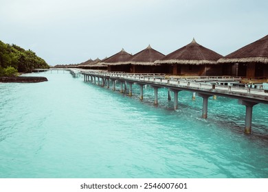 Scenic view of overwater bungalows on stilts extending over turquoise waters, with lush greenery and a tranquil, tropical setting. Ideal for vacation, travel, and relaxation themes. - Powered by Shutterstock