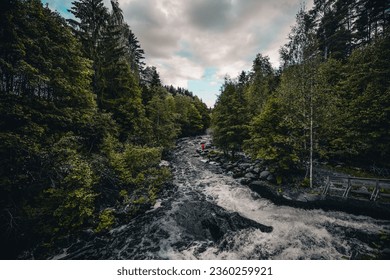 A scenic view of a person standing on rocks in the middle of a river surrounded by greenery - Powered by Shutterstock