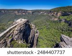 A scenic view from Pulpit Rock lookout platform in the Blue Mountains, New South Wales, Australia. The photo showcases the rugged cliffs and lush greenery of the region.