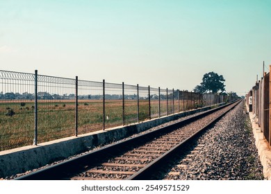 A scenic view of railroad tracks cutting through vibrant green rice fields under a bright, clear sky, representing rural transport - Powered by Shutterstock