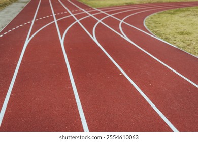 A scenic view of a red running track curving through a grassy field. Ideal setting for athletics, track and field events, and exercise. Perfect for running enthusiasts and sports photography. - Powered by Shutterstock