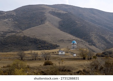 Scenic view of a remote hillside with sparse vegetation and a solitary structure under an overcast sky