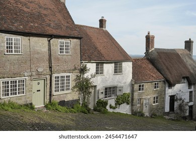 Scenic view of a residential street on a hill with traditional terraced cottage houses in a beautiful English town - namely the landmark Gold Hill in the historic town of Shaftsbury in Dorset England - Powered by Shutterstock