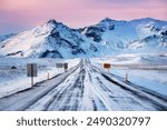 Scenic view from Ring Road Route 1 in Iceland during winter at sunset, with pink clouds, road signs, poles on the side of road, mountains in the background, driving through the beautiful Iceland