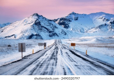 Scenic view from Ring Road Route 1 in Iceland during winter at sunset, with pink clouds, road signs, poles on the side of road, mountains in the background, driving through the beautiful Iceland - Powered by Shutterstock