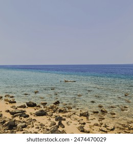 Scenic view of a rocky beach with clear blue water and a small boat floating near the shore - Powered by Shutterstock