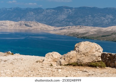 Scenic view of rocky coastline and blue sea with mountains in the background on a sunny day. Concept of outdoor exploration, nature photography, and travel adventure. High quality photo - Powered by Shutterstock