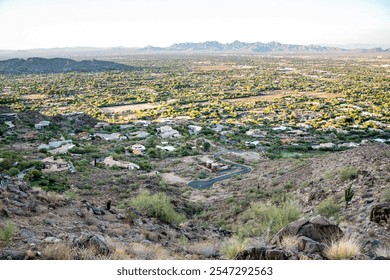 Scenic view from a rocky hillside overlooking a suburban valley with lush greenery and distant mountains under a clear blue sky, showcasing natural beauty and urban harmony - Powered by Shutterstock