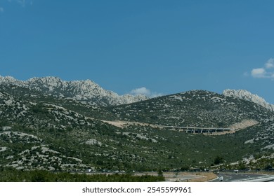 Scenic view of rocky mountain landscape with highway winding through lush green hills under clear blue sky on sunny day. Concept of nature, transportation, and travel in Mediterranean region.  - Powered by Shutterstock