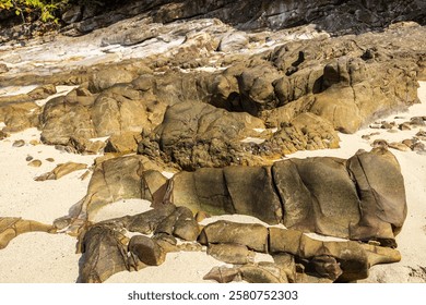 A scenic view of a rocky seashore with sandy patches, rugged cliffs, and vibrant textures, captured under bright sunlight in Koh Jum, Thailand. Ideal for nature and travel imagery.