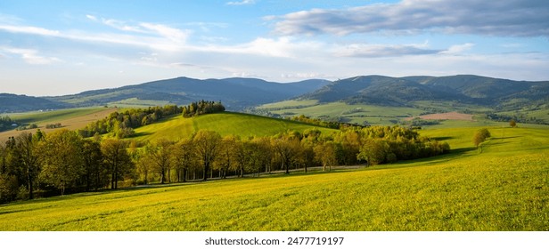 A scenic view of rolling green hills and distant mountains in the Kralicky Sneznik Mountains of Czechia. The landscape is bathed in warm sunlight, creating a serene and peaceful atmosphere. - Powered by Shutterstock