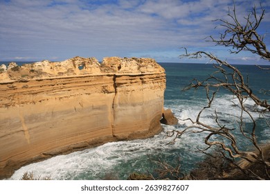 Scenic view of rugged cliffs and ocean waves at Loch Ard Gorge, Great Ocean Road, Australia, under a partly cloudy sky.