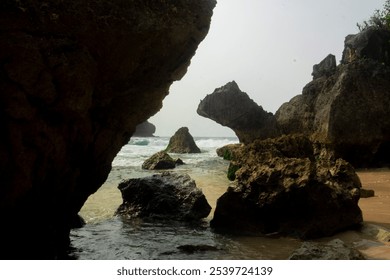 A scenic view of rugged coastal rocks framing the ocean, with waves gently crashing against the shore. This image captures the raw beauty and tranquility of a secluded beach landscape - Powered by Shutterstock