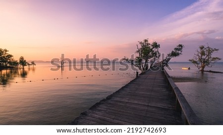 Scenic view of sea with infinity long wooden pier boardwalk bridge over peaceful bay of water in sunset orange sky. Koh Mak Island, Trat Province, Thailand.