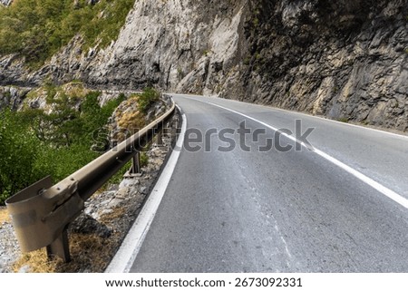 Scenic view of a sharp mountain road turn surrounded by rocky cliffs and greenery, perfectly capturing the natural beauty and adventure of outdoor travel through a picturesque, serene setting