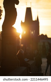 Scenic View With A Silhouette Of A Young Woman Standing With The Back And Reading On Charles Bridge From Prague During An Amazing Autumn Sunrise. Reading In Landmark Places Around The World.