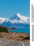 A scenic view of the snowcapped Mount Cook with the blue lake and an asphalt road with cars