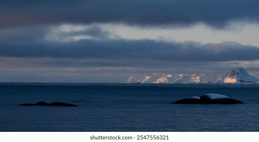 Scenic view of snow-capped mountains under a dramatic sky over the ocean at dawn, capturing the serene beauty of nature. - Powered by Shutterstock