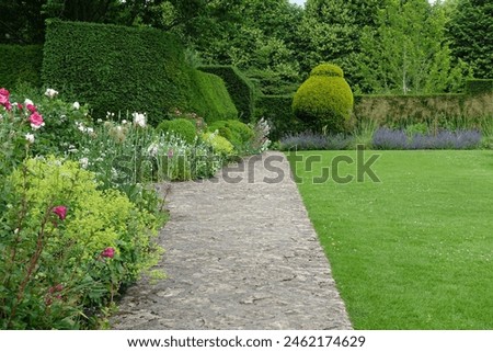 Scenic view of a stone paved path in a beautiful English style landscape garden with a green grass lawn and colourful flowers in bloom - garden themed photograph in colour