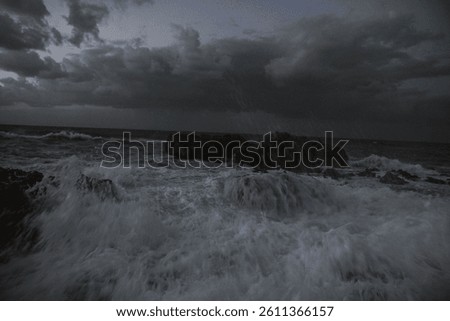 A scenic view of strong waves hitting on a small rocky island under a gloomy sky
