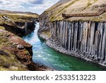 A scenic view of Studlagil Canyon in Iceland with basalt columns and a turquoise river flowing through.