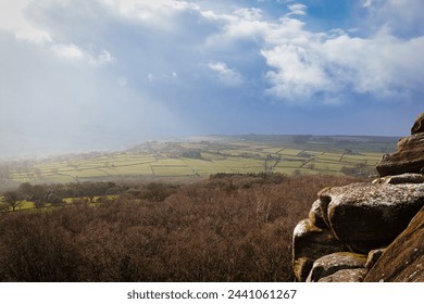 Scenic view of a sunlit countryside landscape with rocky foreground under a dramatic sky at Brimham Rocks, in North Yorkshire