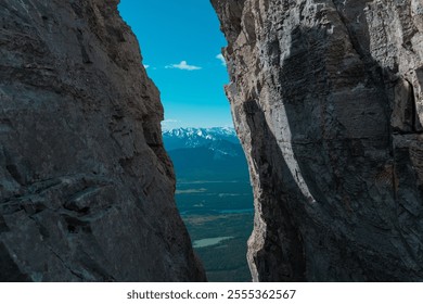 A scenic view through a narrow rock crevice, revealing a distant landscape with mountains and a forest under a clear blue sky. - Powered by Shutterstock