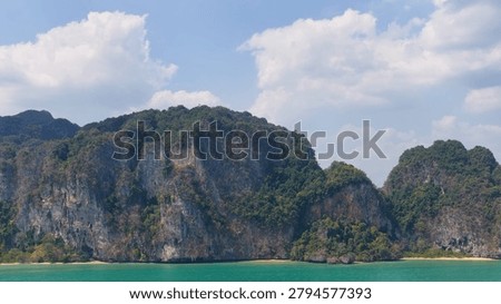 Scenic view of towering limestone cliffs covered in greenery above turquoise Andaman Sea water.