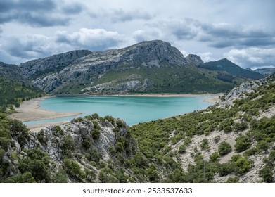 Scenic view of a turquoise lake surrounded by rocky mountains and lush greenery under a cloudy sky. - Powered by Shutterstock