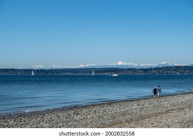 Scenic view of two people walking along the beach at Discovery Park, with the Olympic Mountains in the background