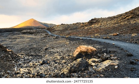 Scenic view of a winding path through a volcanic landscape with a sunlit mountain in the distance at sunset. - Powered by Shutterstock